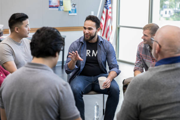 Mid adult Hispanic veteran talks with fellow veterans Mid adult Hispanic male veteran gestures as he discusses something during a veterans group meeting in a community center. group therapy photos stock pictures, royalty-free photos & images