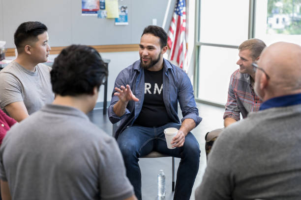 Mid adult Hispanic veteran talks with fellow veterans Mid adult Hispanic male veteran gestures as he discusses something during a veterans group meeting in a community center. veteran military army armed forces stock pictures, royalty-free photos & images