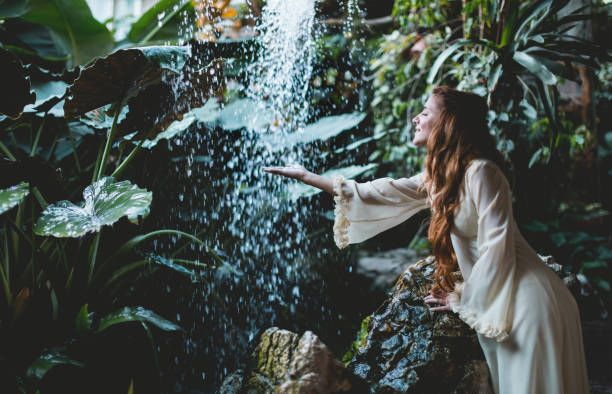 istock Woman in white dress standing against waterfall 1177235197
