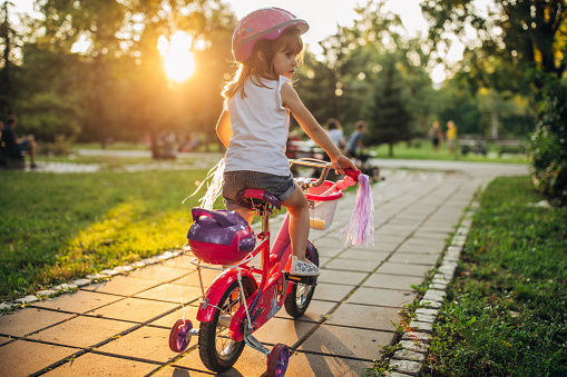 One girl, cute little girl riding a bicycle in park alone.