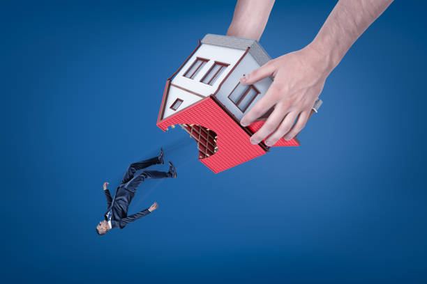 Close-up of man's hands holding house with hole in roof upside down and dropping out little businessman. stock photo