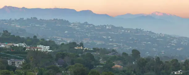 Aerial view of the communities of Bel Air, Benedict Canyon and Holmby Hills at sunset. These exclusive neighborhood on the Westside of Los Angeles are located on the foothills of the Santa Monica Mountains. The San Gabriel mountains of southern California including Mount Baldy  their tallest peak - are in the background.