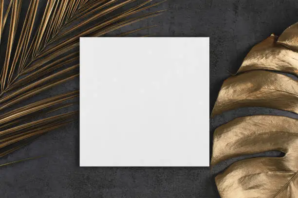 Photo of White square poster or card mockup with golden palm and monstera leaves on dark grey background