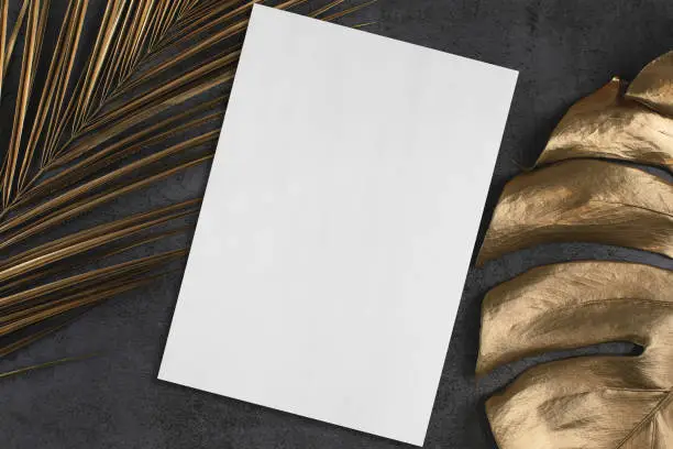 Photo of Empty vertical rectangle poster mockup with golden palm and monstera leaves on dark grey background