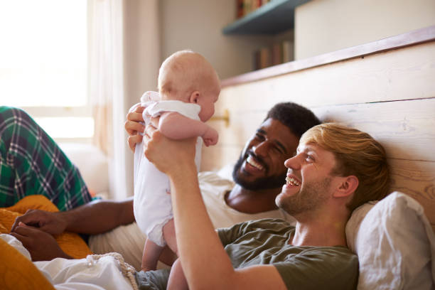 loving male same sex paar kuscheln baby tochter im schlafzimmer zu hause zusammen - homosexuelles paar stock-fotos und bilder