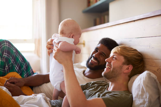 Loving Male Same Sex Couple Cuddling Baby Daughter In Bedroom At Home Together Loving Male Same Sex Couple Cuddling Baby Daughter In Bedroom At Home Together adoption photos stock pictures, royalty-free photos & images