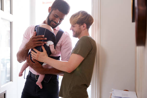Same Sex Male Couple With Baby Daughter In Sling Opening Front Door Of Home Same Sex Male Couple With Baby Daughter In Sling Opening Front Door Of Home civil partnership stock pictures, royalty-free photos & images