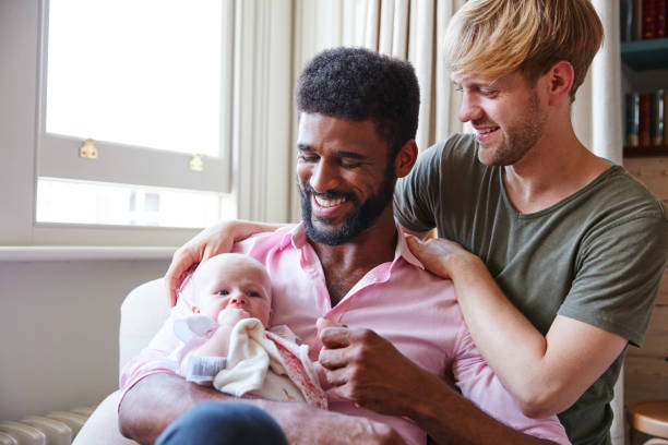 Loving Male Same Sex Couple Cuddling Baby Daughter On Sofa At Home Together Loving Male Same Sex Couple Cuddling Baby Daughter On Sofa At Home Together homosexual couple stock pictures, royalty-free photos & images