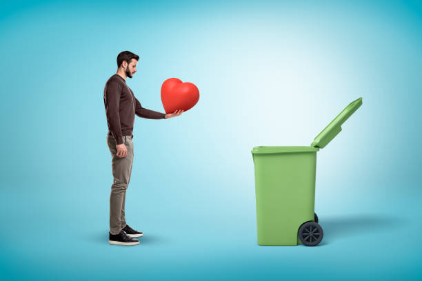 istock Man throwing red heart into open garbage bin on blue background 1177245359