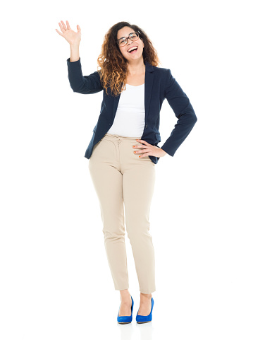 One person / full length / front view / looking at camera of 30-39 years old adult beautiful curly hair / long hair latin american and hispanic ethnicity / puerto rican ethnicity female / young women businesswoman / business person standing in front of white background wearing blazer - jacket / jacket / t-shirt / shirt / pants and high heels who is smiling / happy / cheerful and greeting / showing hand raised / arms outstretched