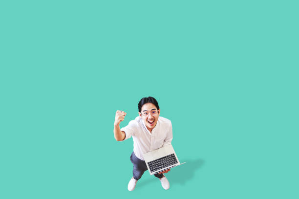 Top view of cheerful asian man holding computer laptop on isolated background feeling win ,celebrating and victory. Young asian man lifestyle concept green background.