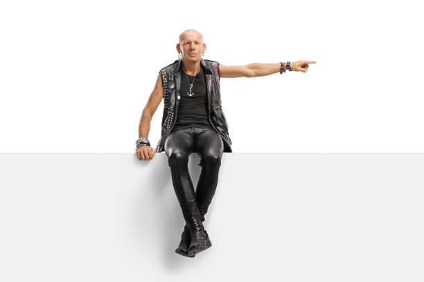 istock Male punk in leather clothes sitting on a panel and pointing to the side 1177261770
