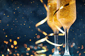 Two glasses of champagne with golden confetti, glitter, serpentine and lights.