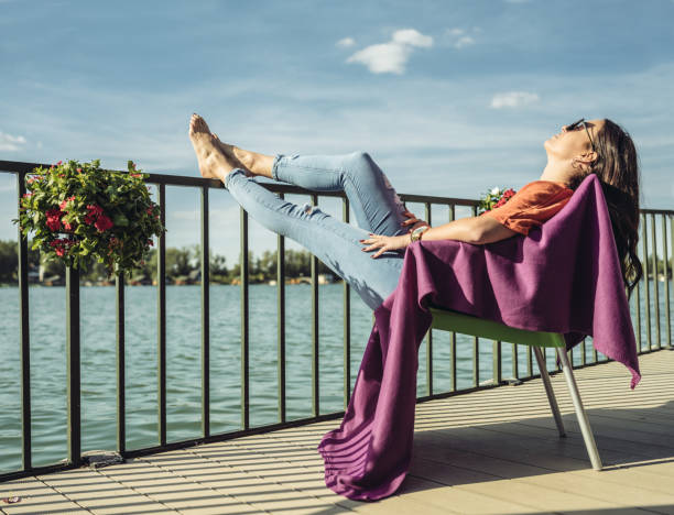 Millennial woman  having fun at the cottage. Suntanning on the terrace, near water. End of the summer weekend.