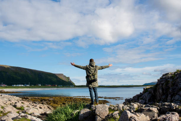 istock A man with messenger bag walking on stone along an empty ocean beach and looking at the mountains. Scenic view. Travel, adventure. Sense of freedom, lifestyle. Lofoten Islands, Norway. North summer 1177265736