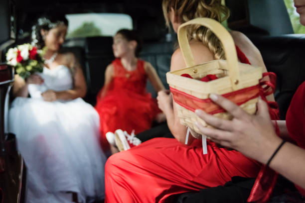 Millennial woman with kids and tattoos on her way for a traditional wedding. Here the focus on the petal basket with the future bride is having a candid moment with her kids in background of the limo car. Horizontal waist up indoors shot with some copy space.