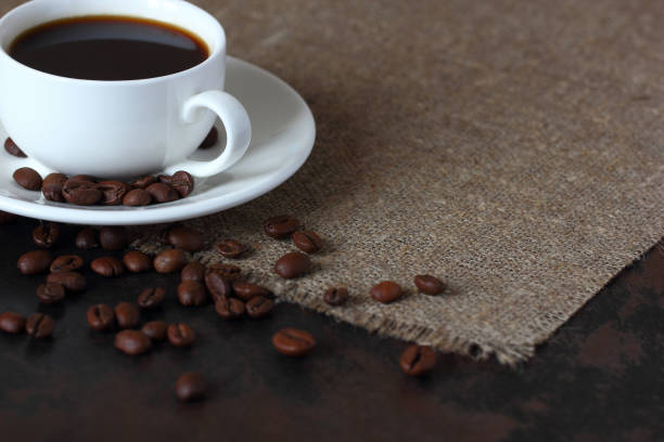 istock Mug with coffee on a saucer and scattered coffee beans on burlap tablecloth. 1177267620