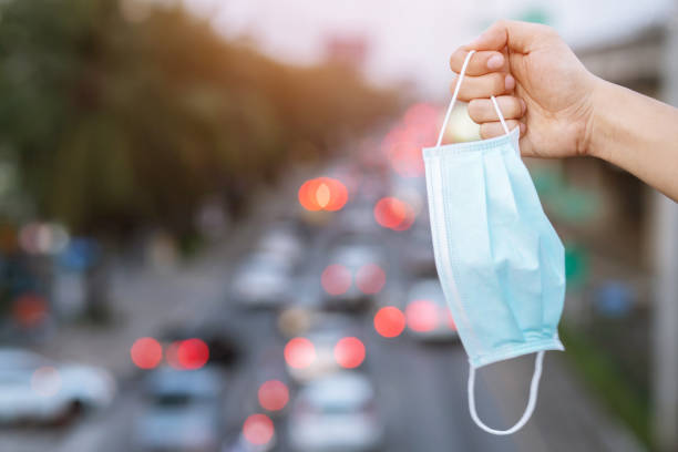 mano ravvicinata tenendo invio indossando naso maschera igienica facciale all'aperto. ecologia, inquinamento atmosferico auto, concetto di protezione ambientale e virus salute influenzale contro le polveri tossiche la città di un effetto sulla salute - air pollution immagine foto e immagini stock