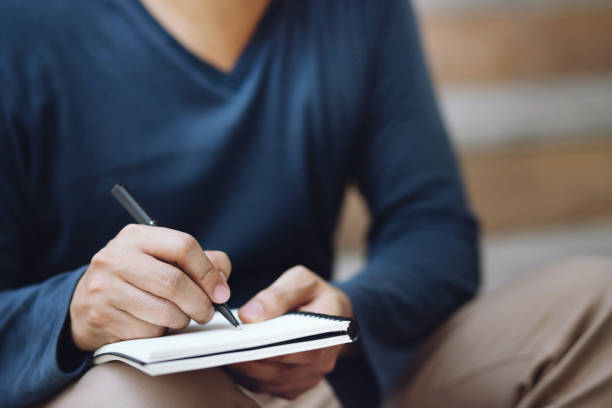 istock close up hand people man are sitting on a chair wooden. using pen writing Record Lecture note pad into the book in park public. Leave space to write descriptive text. 1177269048