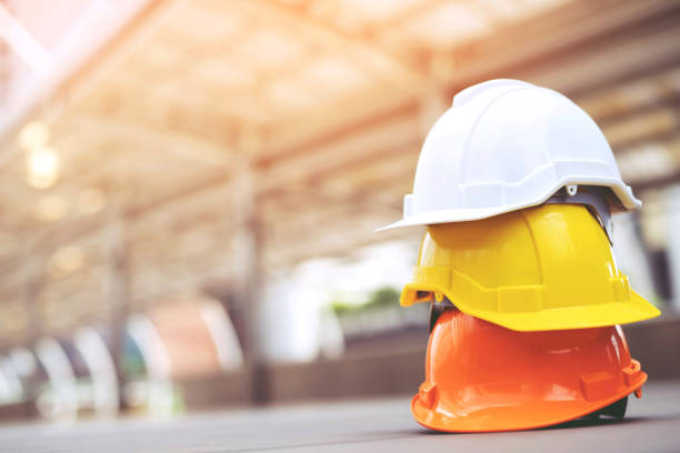 주황색 노란색과 흰색 하드 안전 착용 헬멧 모자 는 햇빛과 도시에 콘크리트 바닥에 건설 현장 건물에서. 엔지니어 또는 노동자로 노동자 헬멧. 개념 안전 제일 - protective workwear hat violence construction 뉴스 사진 이미지
