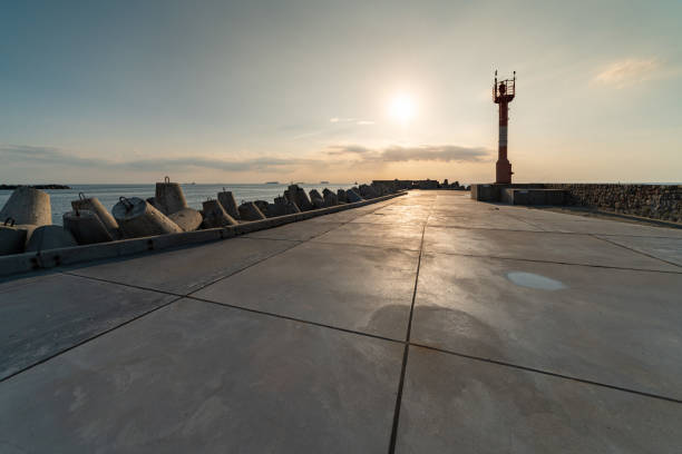 North pier with breakwaters, sunset seascape. Modern lighthouse in sunlight. Tetrapods along edges of pier. Beautiful evening seascape.