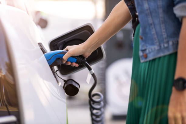 chargement de femme d'une voiture électrique - charger électricité photos et images de collection