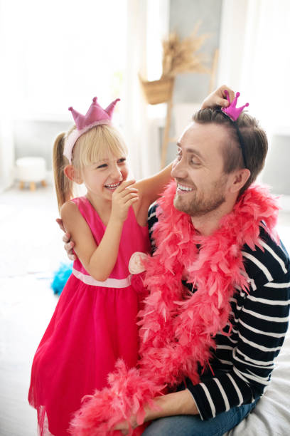 Daughter laughing while giving little crown for daddy Crown for daddy. Daughter wearing pink dress laughing while giving little crown for daddy happy fathers day funny stock pictures, royalty-free photos & images