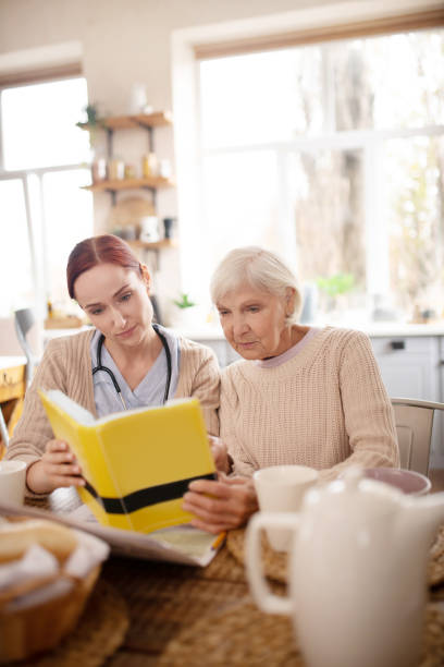 istock Red-haired caregiver reading book for aged lady 1177288072