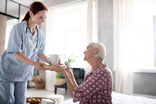 istock Red-haired nurse bringing breakfast for retired woman 1177288166