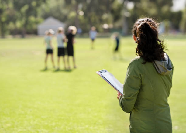 Coach monitoring the team practicing Shot of a female coach with a clipboard watching the team practicing on sports field checking sports stock pictures, royalty-free photos & images