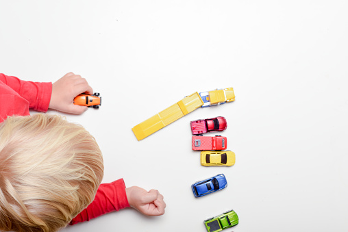 Little blond boy standing by the living room table and playing with toy cars