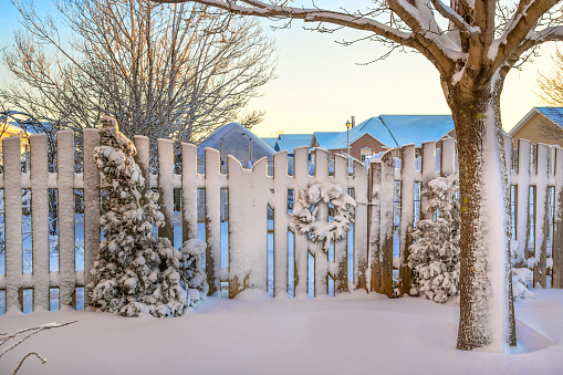 A garden gate decorated with a Christmas wreath all covered in snow.