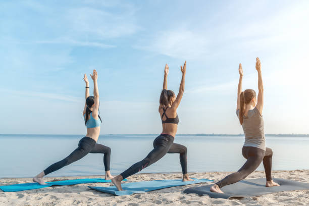plein plan de longueur de cours de yoga à la plage à l'extérieur - yoga class caucasian young adult group of people photos et images de collection