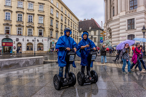 Vienna, Austria - July 13, 2019: Two tourists in raincoats looking at tourist architectural sights on the streets of Vienna, Austria. Autumn weather in Vienna. Segway as a city vehicle