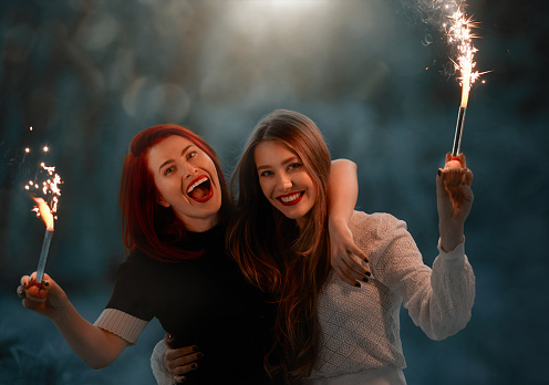 Cheerful best friends celebrating and smiling at the camera, holding sparklers