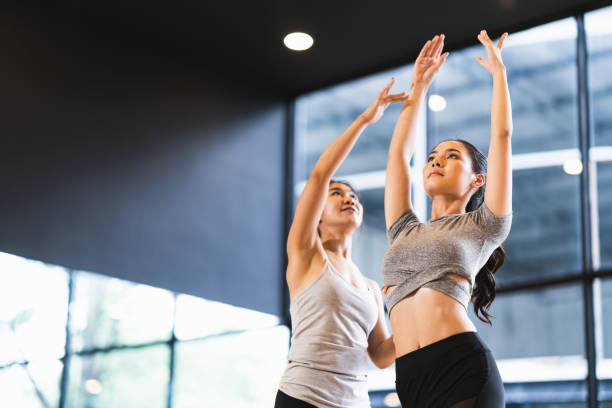 beautiful asian woman learning yoga pose with female instructor in yoga studio or health club. sport exercise activity, gymnastics or ballet dancing class, or healthy people lifestyle concept - instructor exercising gym women imagens e fotografias de stock