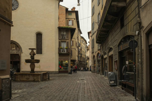 una calle y una pequeña plaza con fuente en la zona histórica, o casco antiguo, en bérgamo, italia - architecture bergamo blue building exterior fotografías e imágenes de stock