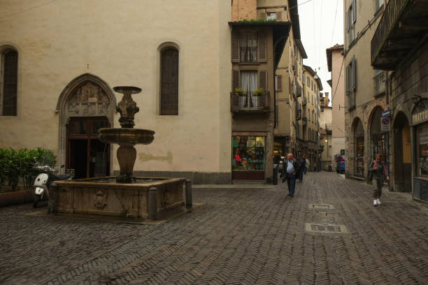 una calle y una pequeña plaza con fuente en la zona histórica, o casco antiguo, en bérgamo, italia - architecture bergamo blue building exterior fotografías e imágenes de stock