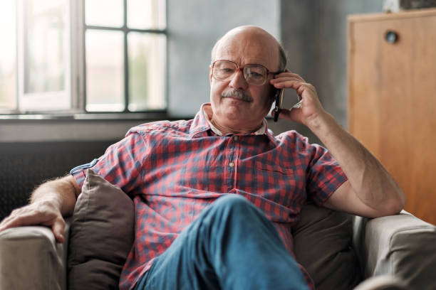 пенсионер испаноязычных человек разговаривает по телефону, сидя в гостиной. - telephone worried one person discussion стоковые фото и изображения