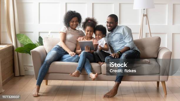 African Full Family Using Tablet Computer Resting On Couch Stock Photo - Download Image Now