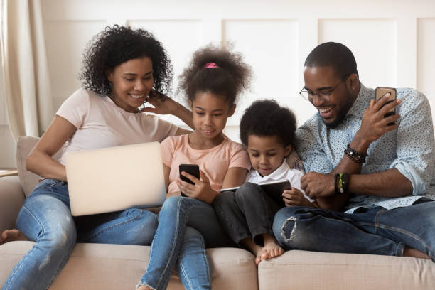 famille africaine et gosses utilisant différents gadgets s'asseyant sur le divan - digital tablet women enjoyment happiness photos et images de collection