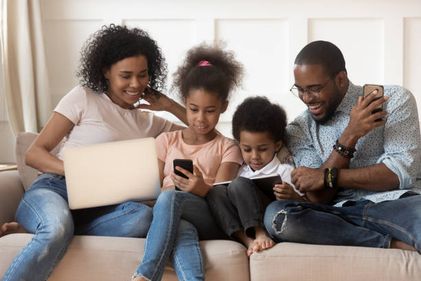 família africana e miúdos que usam dispositivos diferentes que sentam-se no sofá - digital tablet family father offspring - fotografias e filmes do acervo