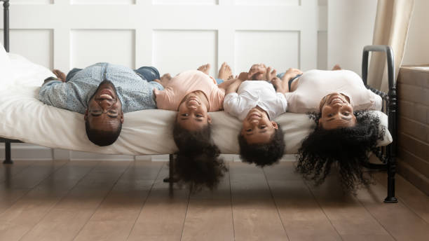 afrikanische familie liegt auf bett köpfen nach unten und schaut auf die kamera - women group of people lying down mother stock-fotos und bilder