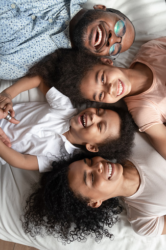 Close up vertical portrait view from top african couple small kids laughing lying down on bed, family stable relationships high degree of trust, connection protection happy family is happiness concept