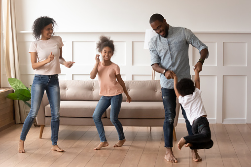Full length of active energetic african family standing in living room barefoot enjoy warm floors celebrating new property real estate modern home purchase or foretastes vacations feels happy concept