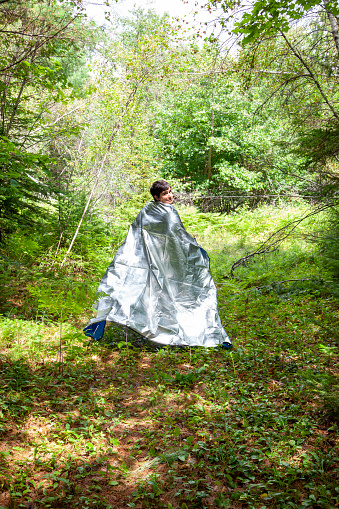 person freely running in the forest with an insulated silver blanket