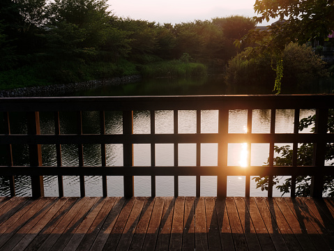 Beautiful sunset with the reflection on the water surface seen from wooden deck with fence