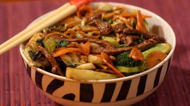 Asian dish yakisoba served in a bowl with sticks on top close up