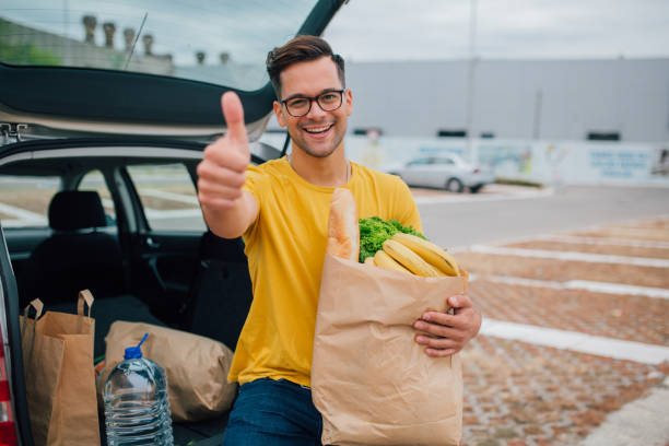 istock Young man holding grocery bag while sitting in cur trunk and showing thumbs up 1177329526