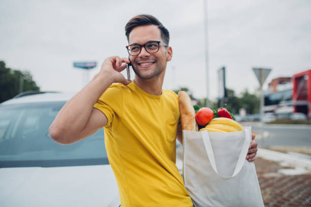 istock Young man using phone and holding groceries in reusable bag 1177331059